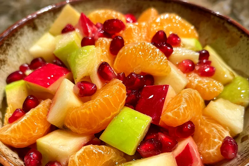 A colorful bowl of Festive Winter Fruit Medley being served at a festive gathering.